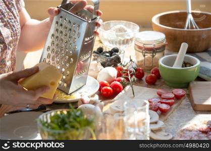 Woman cooking pizza at home. Unrecognizable woman grating cheese
