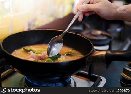 Woman cooking pork noodle soup at kitchen gas stove