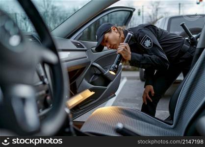 Woman cop using pocket lamp for car examining. Checking detail of automotive traffic accident. Woman cop using flashlight for car examining