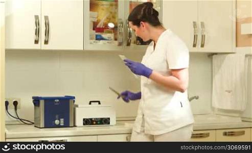 Woman cosmetician putting cosmetological instrument into sterilizer, setting time and starting up sterilization
