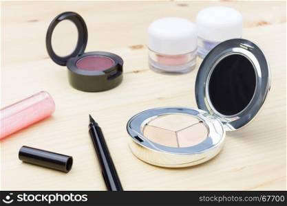 Woman cosmetics include eyes liner and lip gloss, and eyeshadow and foundation or face powder on wood table