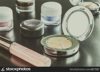 Woman cosmetics include lip gloss and eyeshadow and foundation or face powder on black floor classic style