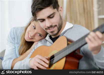 woman cuddling into her boyfriend as he plays the guitar