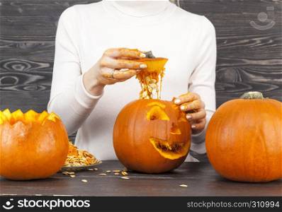 Woman cut a pumpkin for the celebration of Halloween, several small sized orange pumpkins on the table. Woman cut out a pumpkin