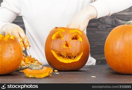 Woman cut a pumpkin for the celebration of Halloween, several small sized orange pumpkins on the table. Woman cut out a pumpkin