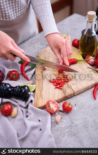 Woman cuts Fresh red chili peppers wooden cutting board at domestic kitchen.. Woman cuts Fresh red chili peppers wooden cutting board at domestic kitchen