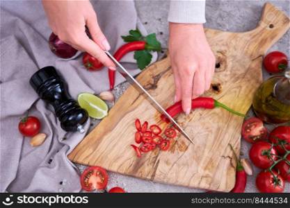 Woman cuts Fresh red chili peppers wooden cutting board at domestic kitchen.. Woman cuts Fresh red chili peppers wooden cutting board at domestic kitchen