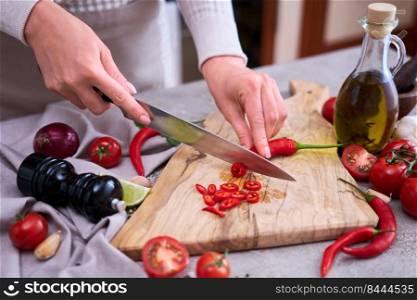 Woman cuts Fresh red chili peppers wooden cutting board at domestic kitchen.. Woman cuts Fresh red chili peppers wooden cutting board at domestic kitchen