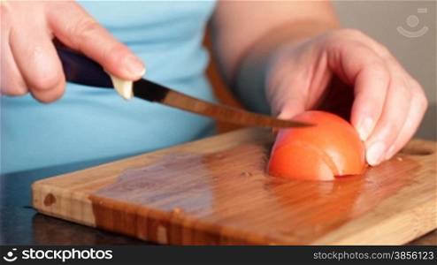 woman cuts tomato for salad.