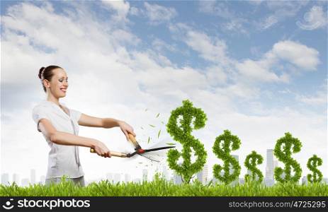 Woman cutting bush. Young happy businesswoman cutting bush shaped like dollar. Income concept