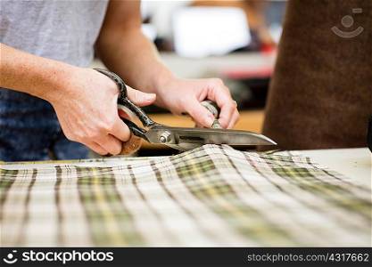 Woman cutting fabric in leather jacket manufacturers, close-up