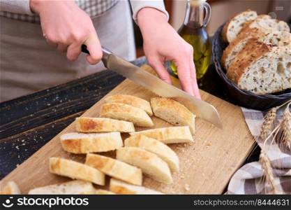 Woman cutting freshly baked bread at wooden kitchen table.. Woman cutting freshly baked bread at wooden kitchen table