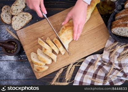 Woman cutting freshly baked bread at wooden kitchen table.. Woman cutting freshly baked bread at wooden kitchen table