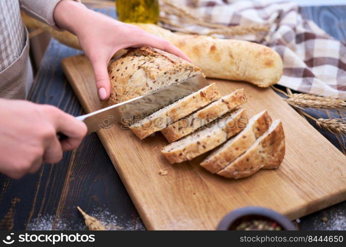 Woman cutting freshly baked bread at wooden kitchen table.. Woman cutting freshly baked bread at wooden kitchen table