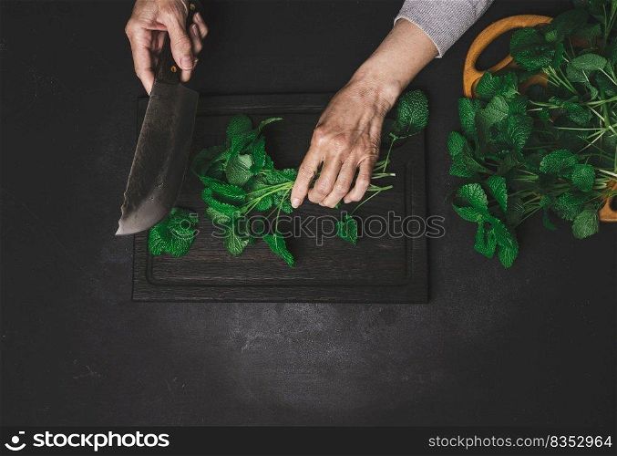 Woman cutting green mint leaves on brown wooden cutting board, top view