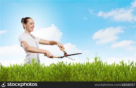 Woman cutting lawn. Young happy businesswoman cutting bush with grass cutter