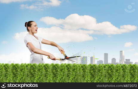 Woman cutting lawn. Young happy businesswoman cutting bush with grass cutter