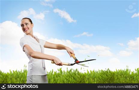 Woman cutting lawn. Young happy businesswoman cutting bush with grass cutter