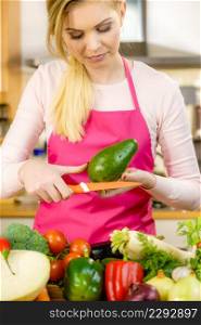 Woman cutting, preparing green vegetable, delicious avocado using kitchen knife. Female wearing apron making food.. Woman cutting avocado
