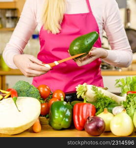 Woman cutting, preparing green vegetable, delicious avocado using kitchen knife. Female wearing apron making food.. Woman cutting avocado