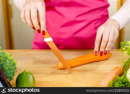 Woman cutting, preparing vegetable, delicious sweet carrot using kitchen knife. Female hands making food.. Woman cutting carrot on kitchen board