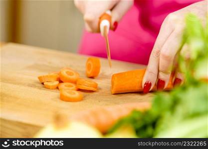 Woman cutting, preparing vegetable, delicious sweet carrot using kitchen knife. Female hands making food.. Woman cutting carrot on kitchen board