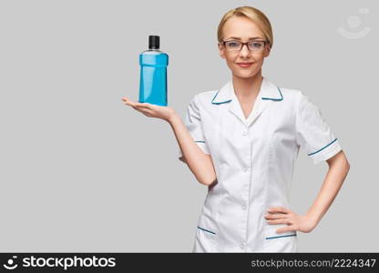 woman dentist doctor holding bottle of mouthwash standing over grey background.. woman dentist doctor holding bottle of mouthwash standing over grey background