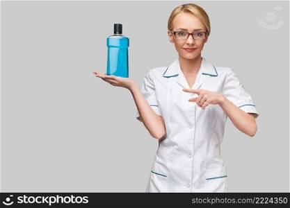 woman dentist doctor holding bottle of mouthwash standing over grey background.. woman dentist doctor holding bottle of mouthwash standing over grey background