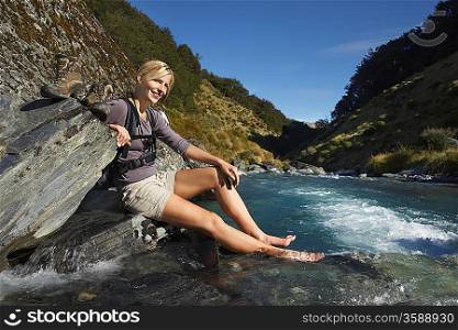 Woman dipping her feet in river in forest valley