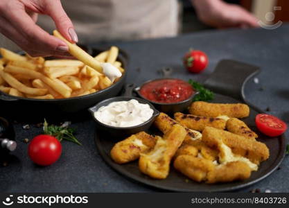 Woman dips french fries into dip sauce with Cheese fried mozzarella sticks on a table.. Woman dips french fries into dip sauce with Cheese fried mozzarella sticks on a table