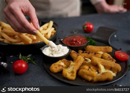 Woman dips french fries into dip sauce with Cheese fried mozzarella sticks on a table.. Woman dips french fries into dip sauce with Cheese fried mozzarella sticks on a table