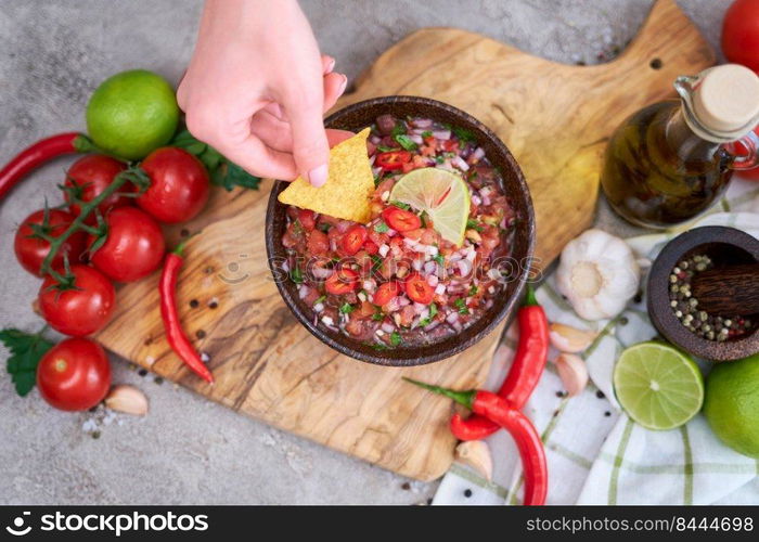 woman dips nacho chip into freshly made salsa dip sauce.. woman dips nacho chip into freshly made salsa dip sauce