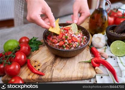 woman dips nacho chip into freshly made salsa dip sauce.. woman dips nacho chip into freshly made salsa dip sauce