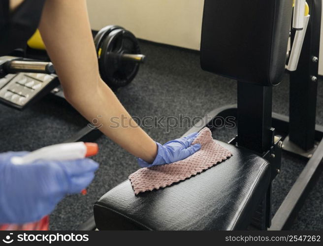 woman disinfecting gym equipment while wearing gloves