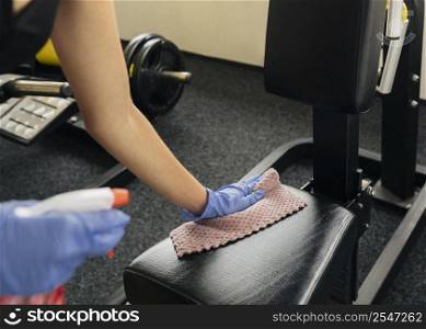 woman disinfecting gym equipment while wearing gloves