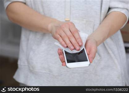 Woman disinfecting phone with antiseptic wet wipe. Antiseptic napkin to prevent spread of germs, bacteria and coronavirus. Coronavirus prevention. Prevent illness coronavirus after public place.