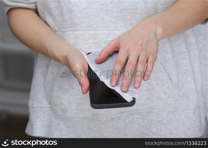 Woman disinfecting phone with antiseptic wet wipe. Antiseptic napkin to prevent spread of germs, bacteria and coronavirus. Coronavirus prevention. Prevent illness coronavirus after public place.