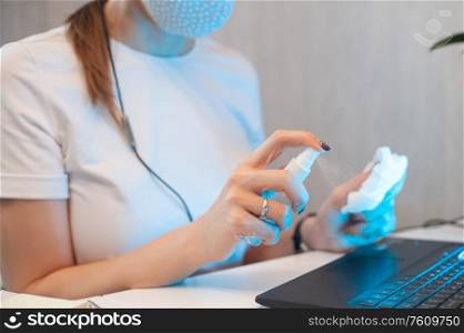 Woman disinfects the surface of the phone by sanitizer spray on the working place.. Woman disinfects the surface of the phone