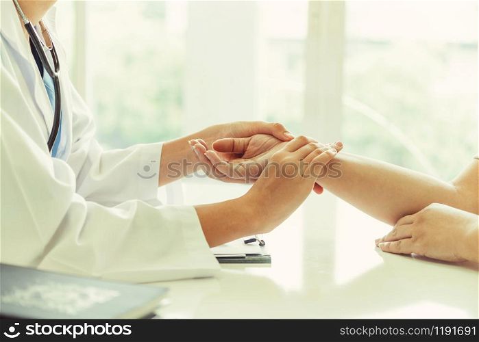 Woman doctor talks to female patient in hospital office while examining the patients pulse by hands. Healthcare and medical service.. Woman Doctor and Female Patient in Hospital Office