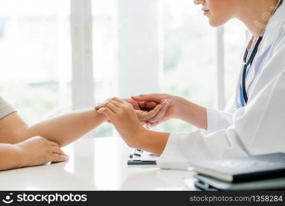 Woman doctor talks to female patient in hospital office while examining the patients pulse by hands. Healthcare and medical service.