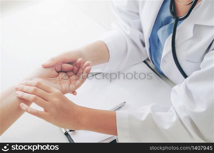 Woman doctor talks to female patient in hospital office while examining the patients pulse by hands. Healthcare and medical service.. Woman Doctor and Female Patient in Hospital Office