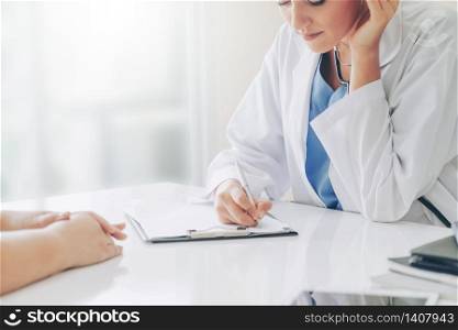 Woman doctor talks to female patient while writing on the patient health record in hospital office. Healthcare and medical service.. Woman Doctor and Female Patient in Hospital Office