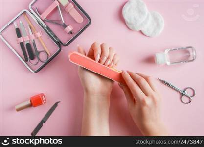 Woman does a manicure at home. Hands with a nail file on a pink background.. Woman does a manicure at home. Hands with a nail file on pink background.