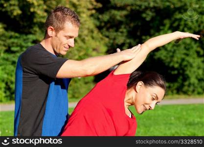 Woman does outdoor stretching with her personal trainer on a great summer day