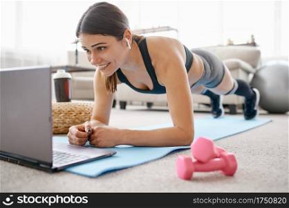 Woman doing abs exercise, online fit training at the laptop. Female person in sportswear, internet sport workout, room interior on background. Woman doing abs exercise, online fit training