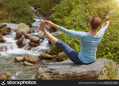 Woman doing Ashtanga Vinyasa asana Upavistha Konasana outdoors at tropical waterfall. Woman doing yoga outdoors