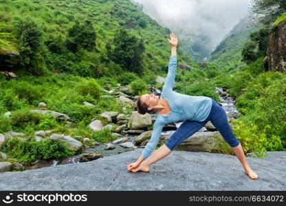 Woman doing Ashtanga Vinyasa yoga asana Utthita trikonasana - extended triangle pose outdoors at waterfall in Himalayas. Woman doing Ashtanga Vinyasa yoga asana Utthita trikonasana