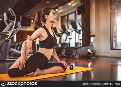Woman doing bending legs yoga in fitness workouts training gym center background. Lifestyle woman sitting with sport dumbbell equipment and exercise treadmill background. Yoga girl in black sports bra