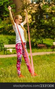 Woman doing exercise outdoor in park, using gym accessory, resistance band. Staying fit and healthy.. Girl doing exercises outdoor, using resistance fit band.