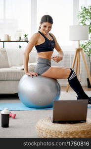 Woman doing exercise with ball, online pilates training at the laptop. Female person in sportswear, internet sport workout, room interior on background. Woman with ball, online pilates training